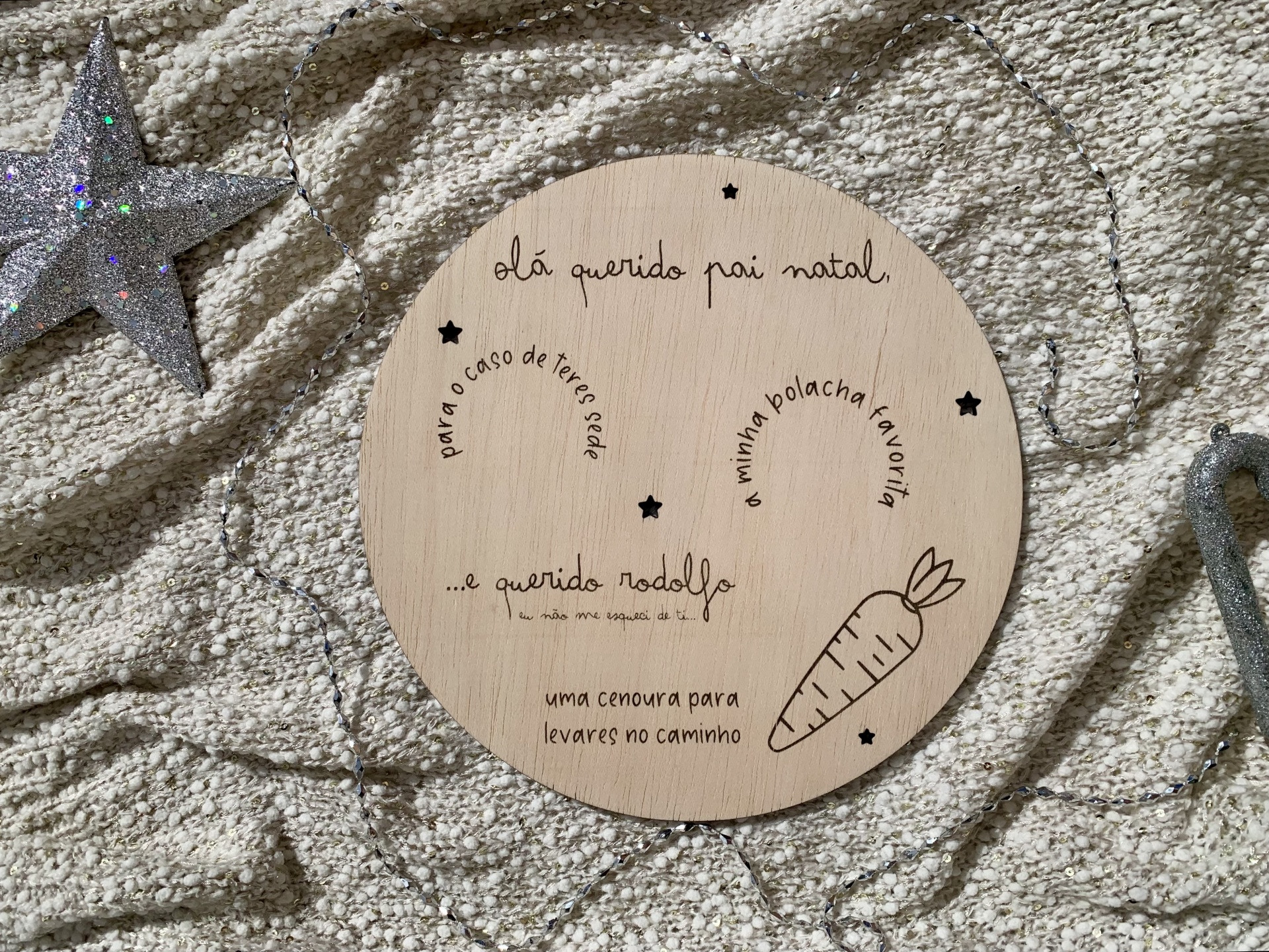 Placa redonda de madeira com texto e desenhos gravados em preto sobre tecido bege com textura e estrela prateada ao lado