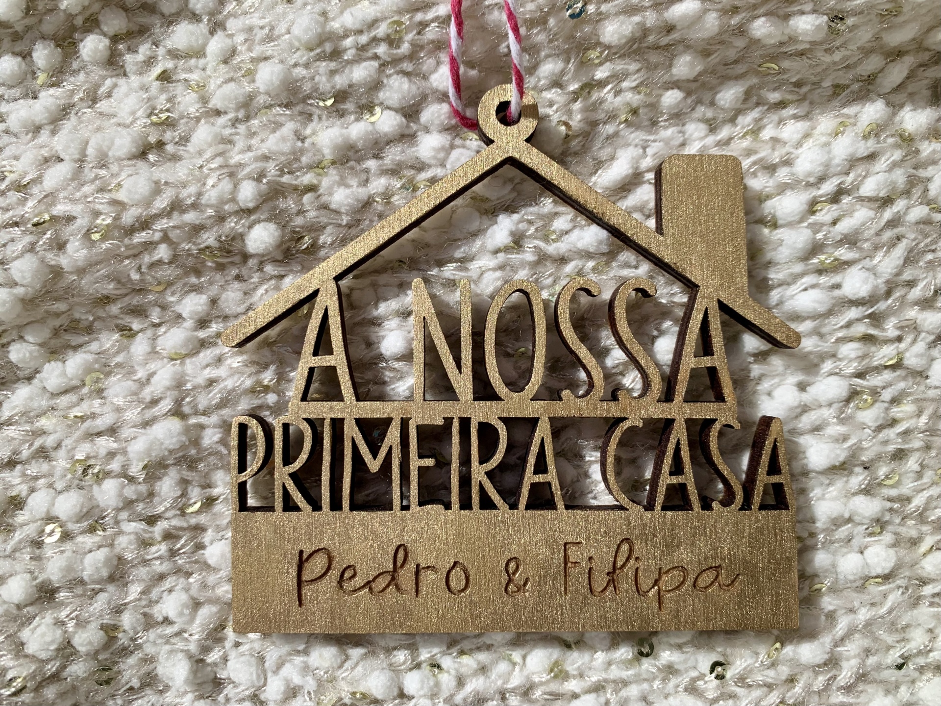 Ornamento decorativo de madeira em forma de casa com texto A NOSSA PRIMEIRA CASA e nomes Pedro & Filipa