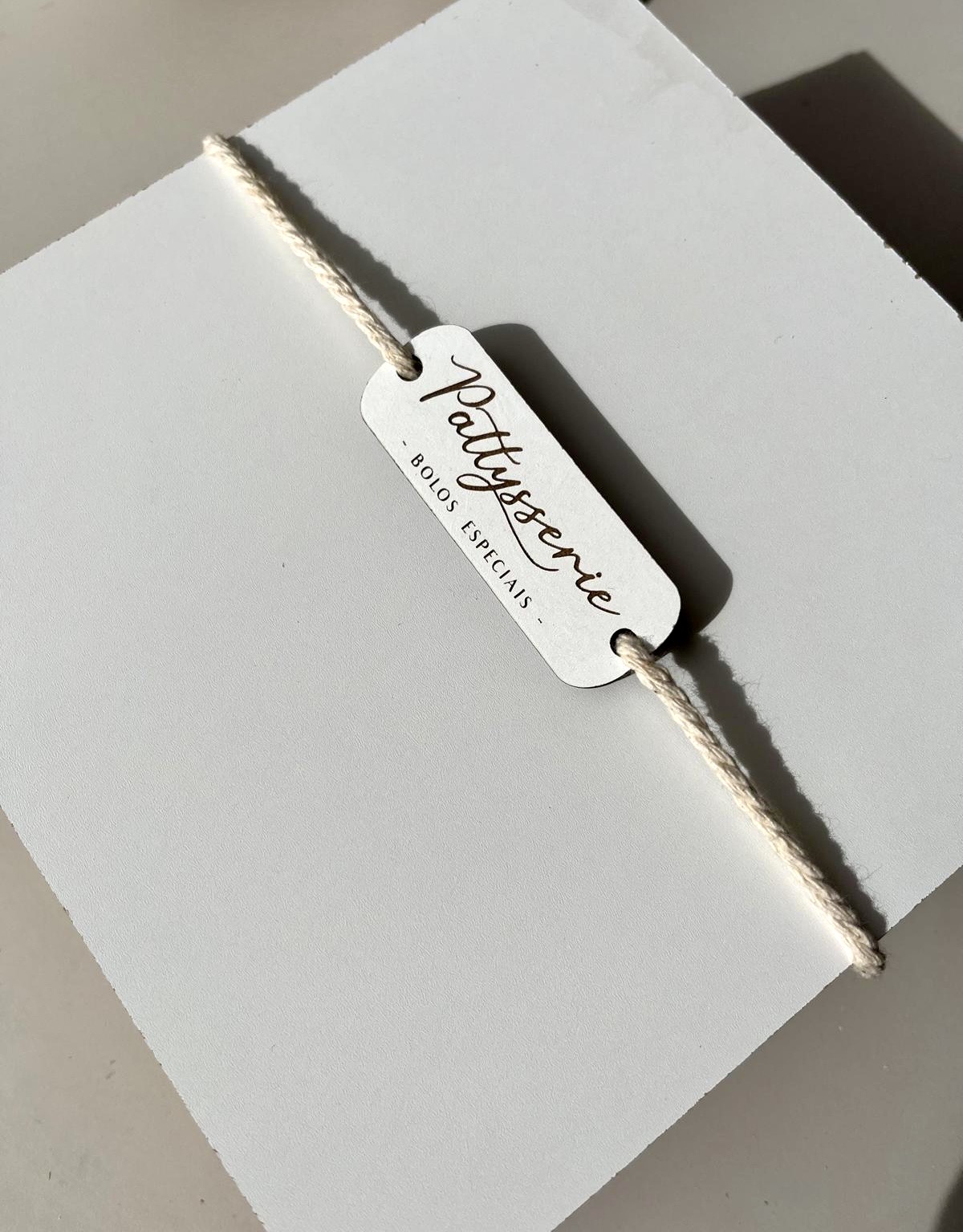 Etiqueta branca com texto Pattysserie - BOLOS ESPECIAIS - presa a corda bege claro