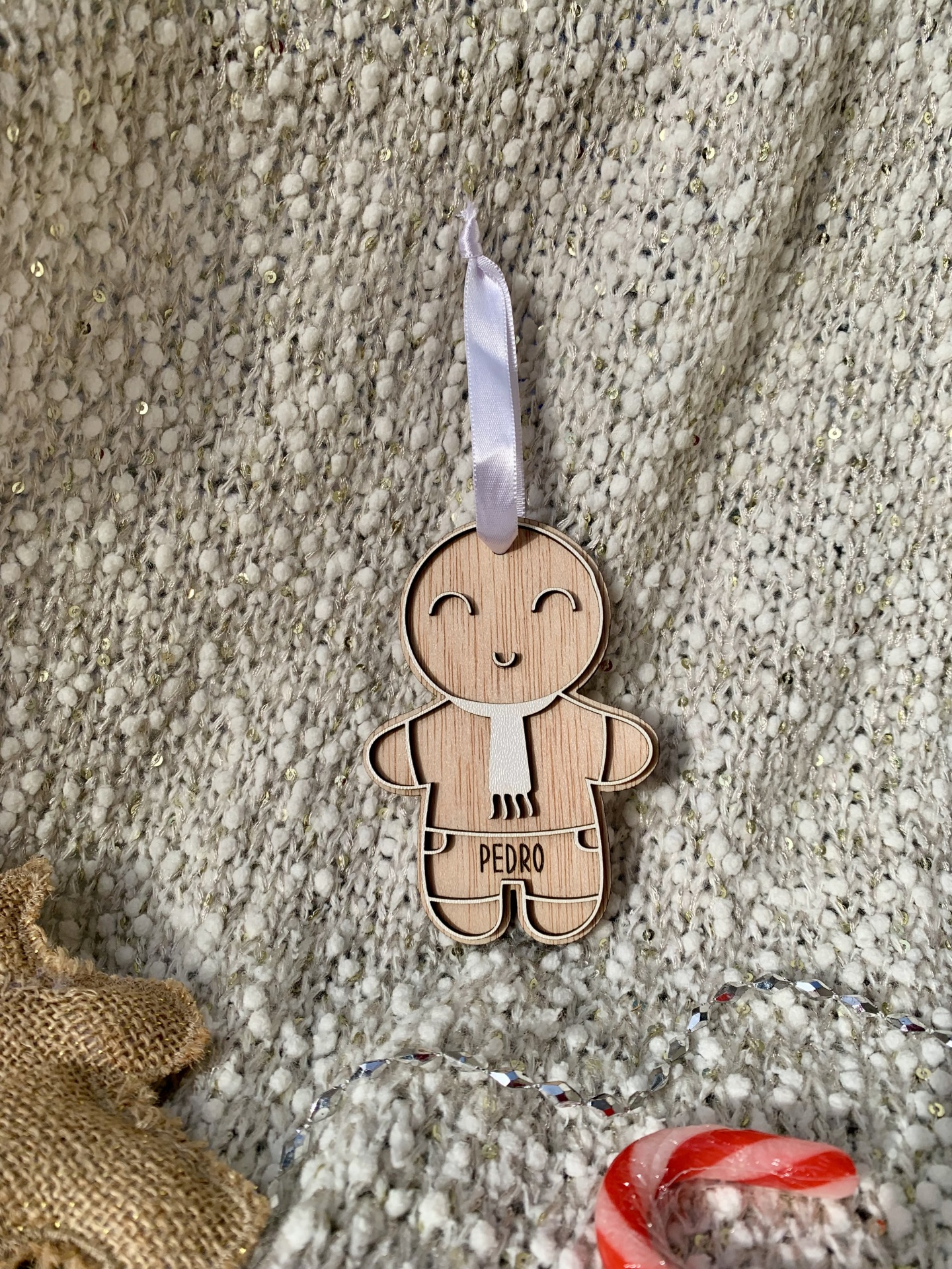 Boneco de madeira decorativo com o nome PEDRO e lenço branco pendurado sobre tecido texturado branco com lantejoulas