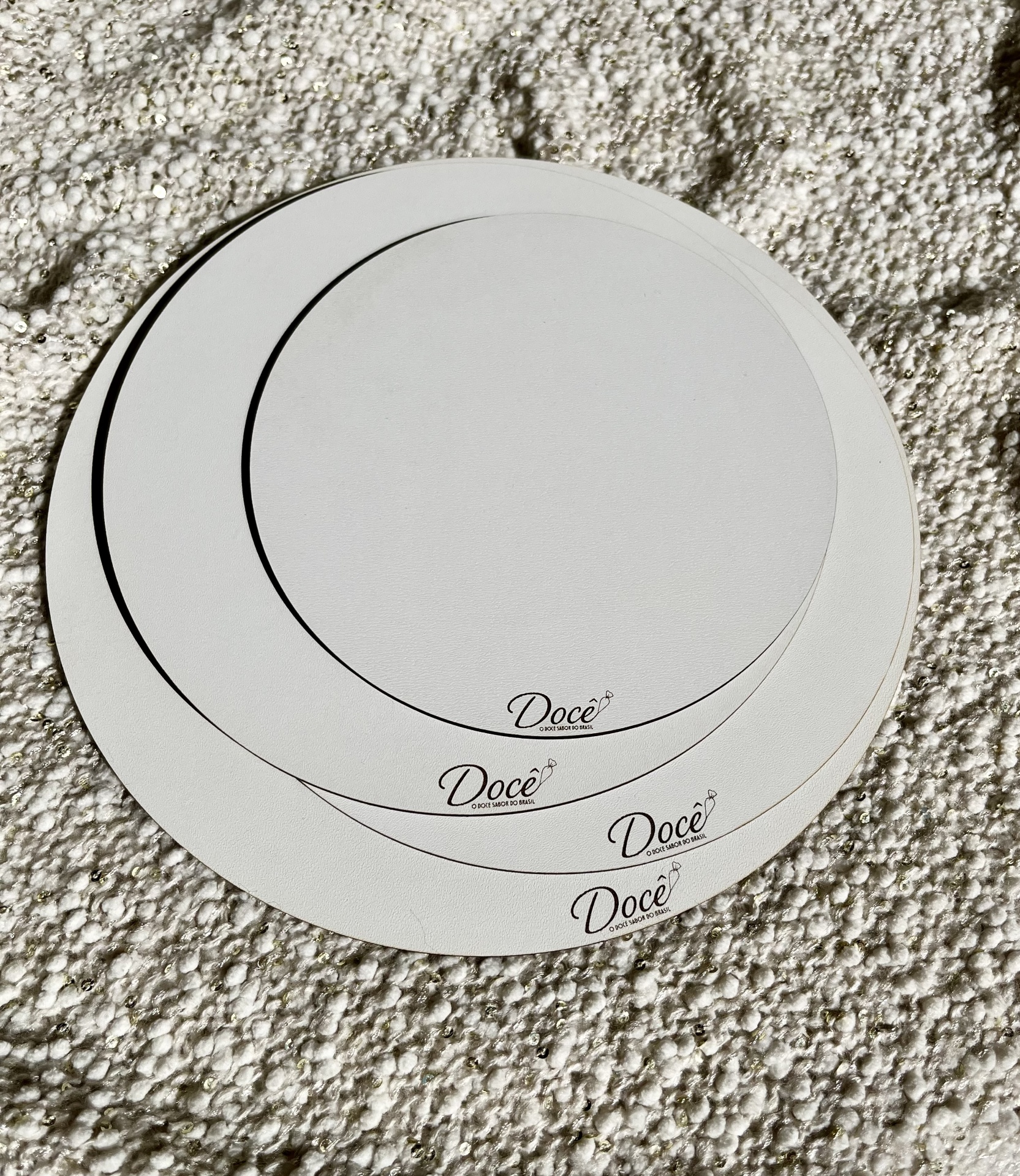 Bases redondas brancas com logo Docê sobre tapete bege