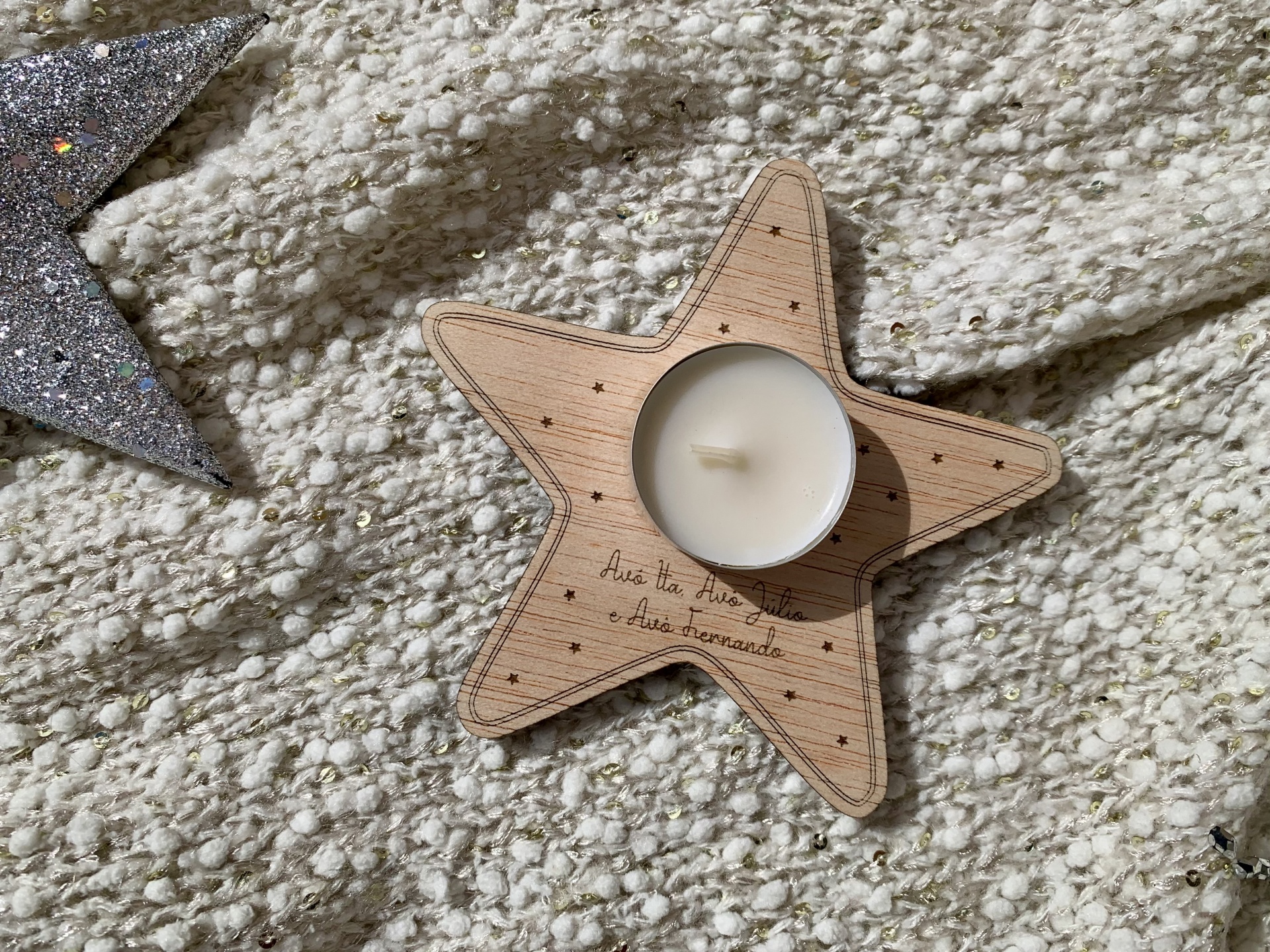 Vela branca numa base de madeira em forma de estrela sobre tecido bege texturado