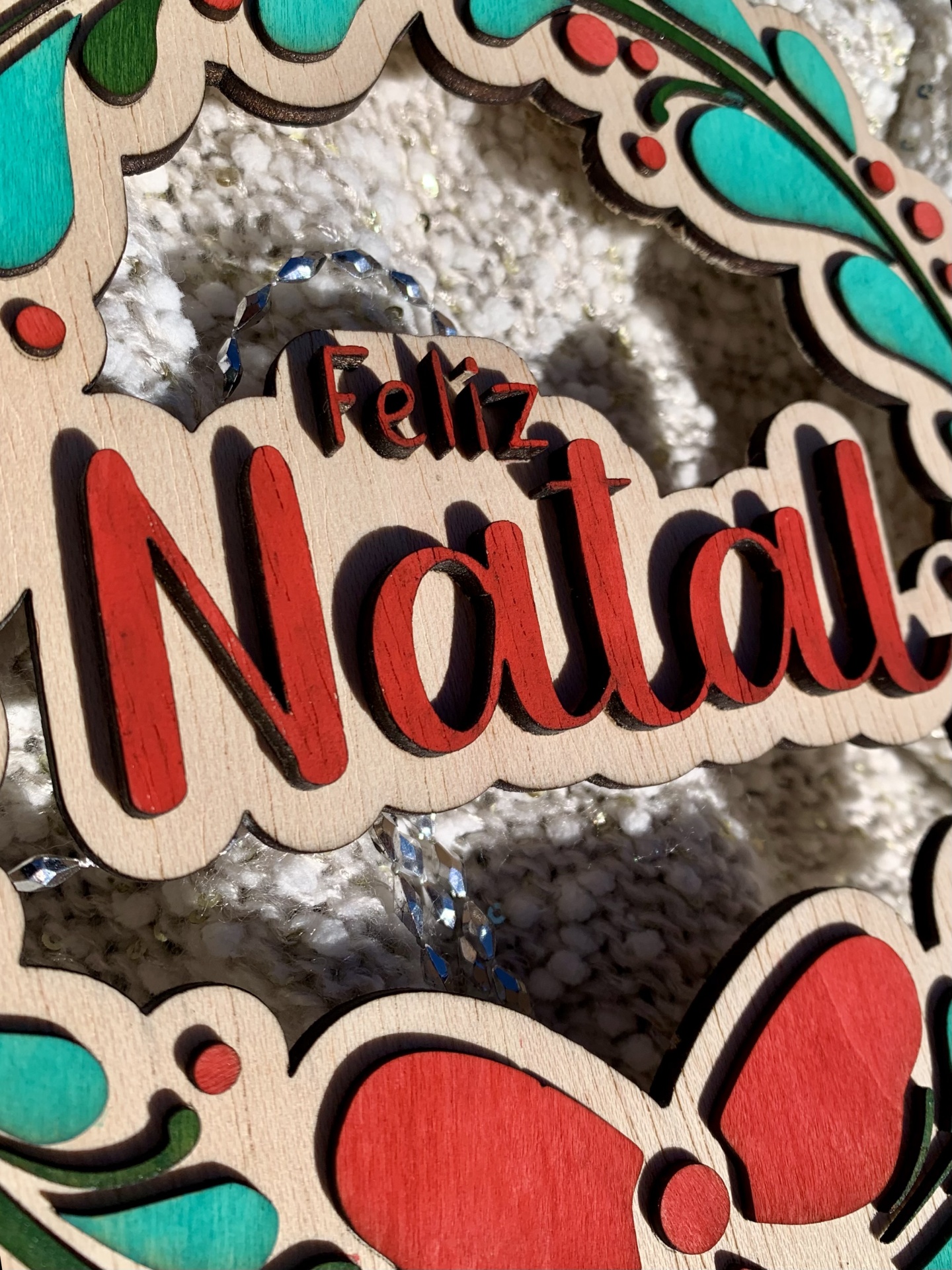 Guirlanda de madeira com texto 'Feliz Natal' em relevo e detalhes coloridos