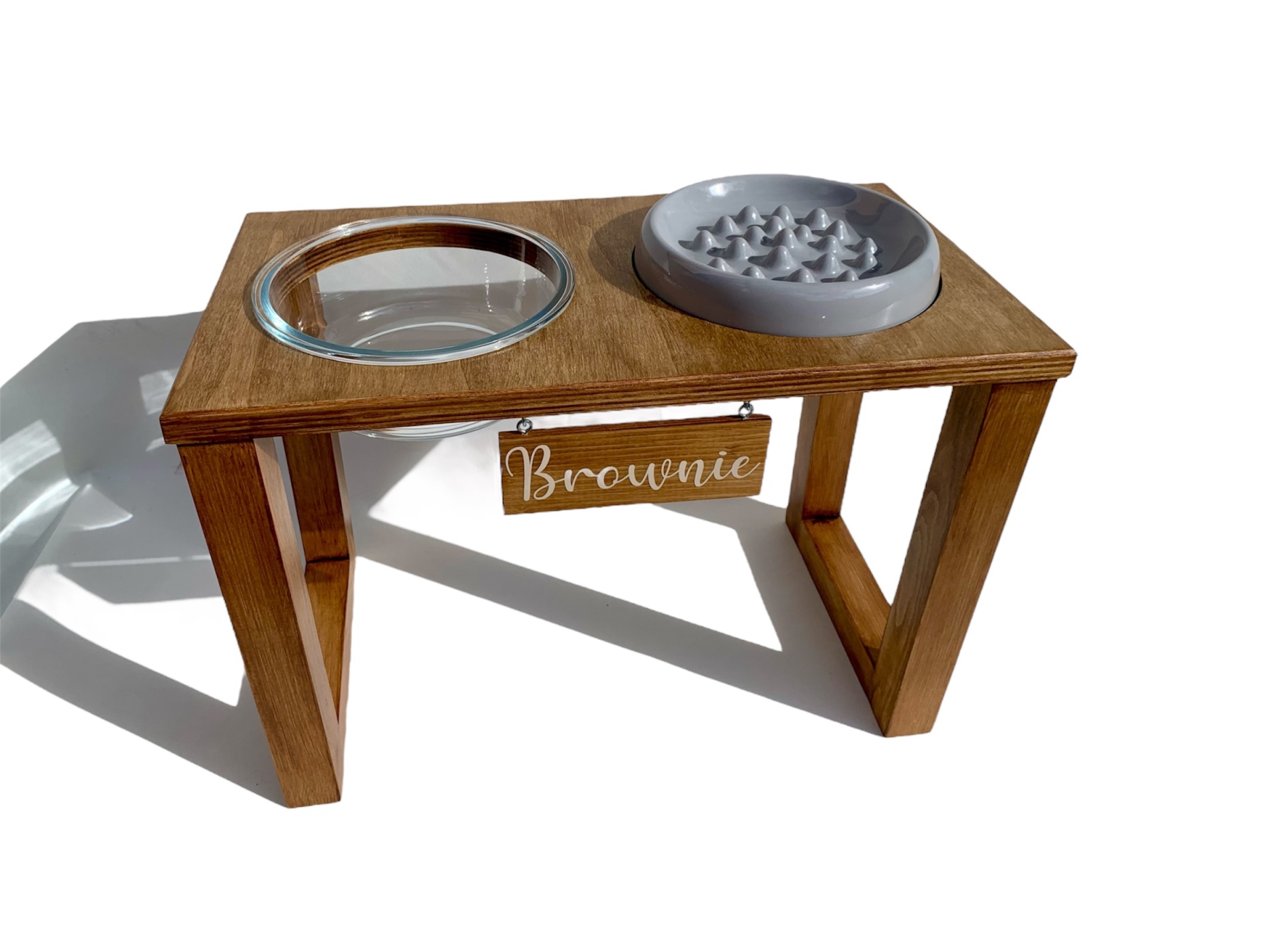 Suporte em madeira com dois comedouros para animais, um vidro e um plástico cinzento, e placa com nome Brownie.