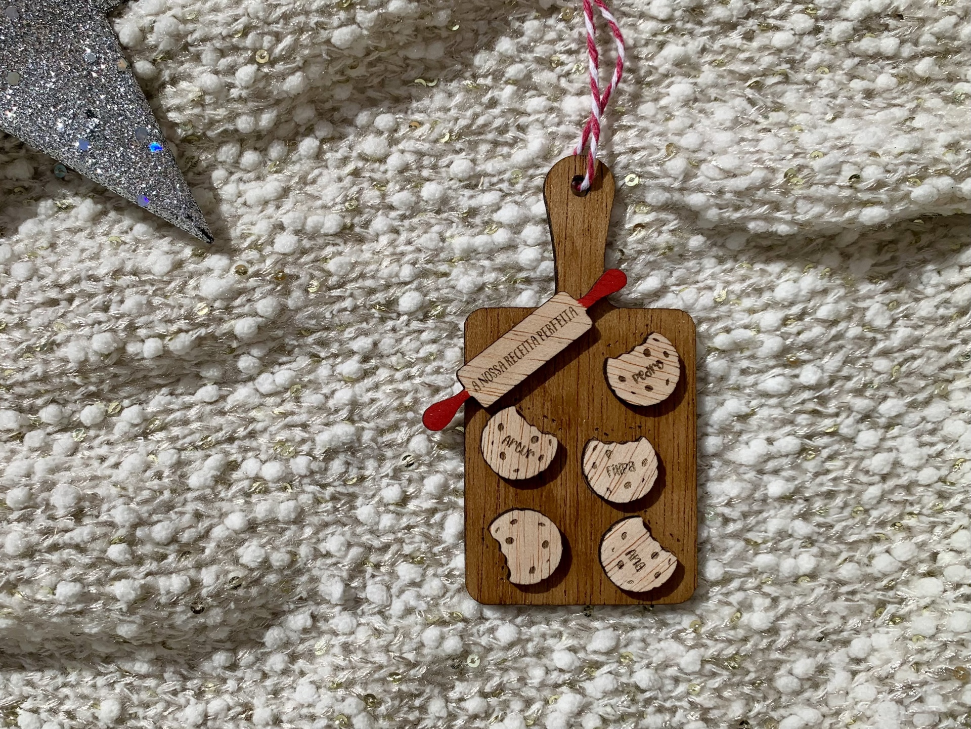 Enfeite decorativo em madeira com cookies e rolo de massa pendurado sobre tapete claro texturizado