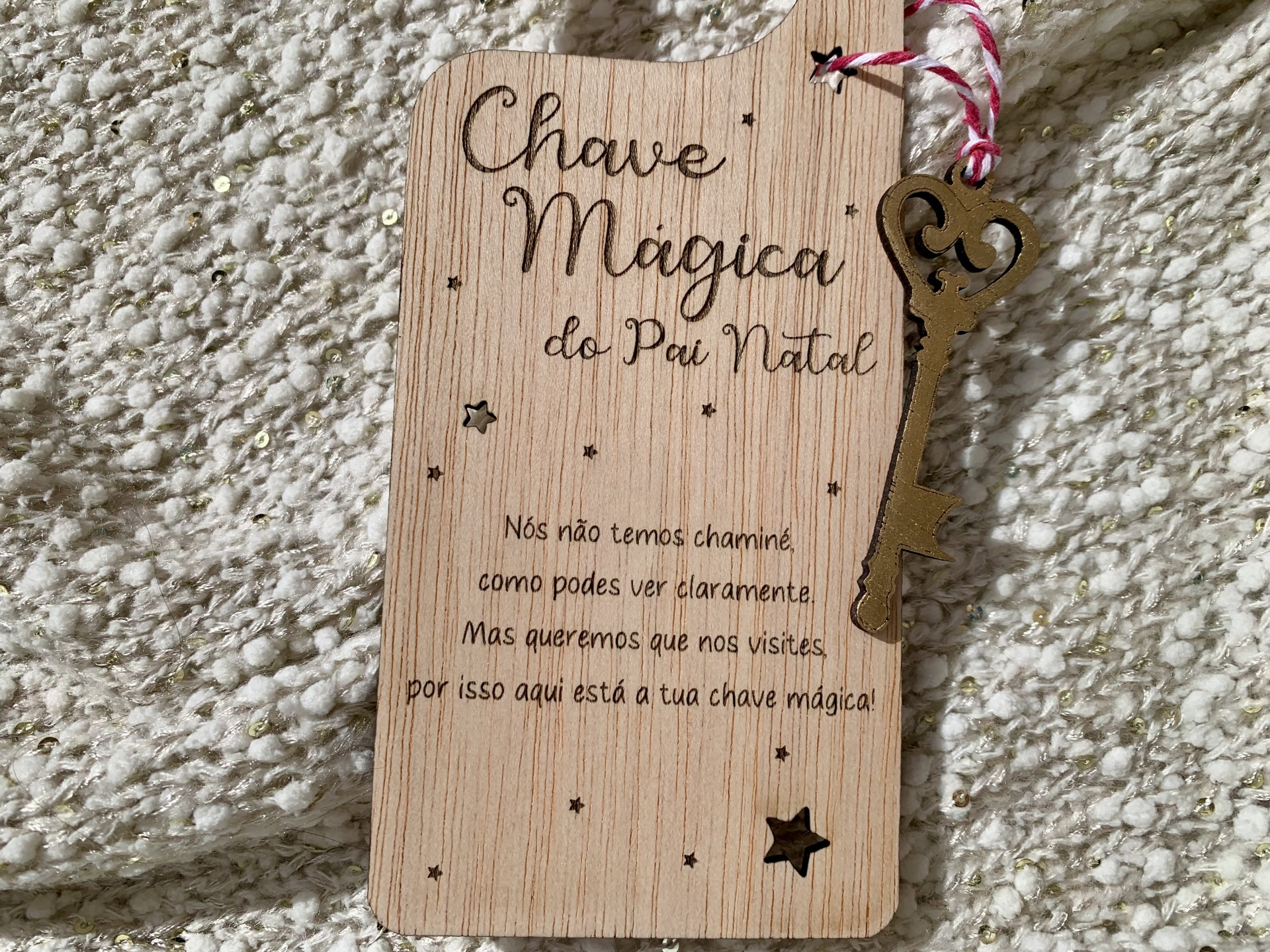 Placa de madeira com chave metálica pendurada e texto gravado que menciona chave mágica do Pai Natal