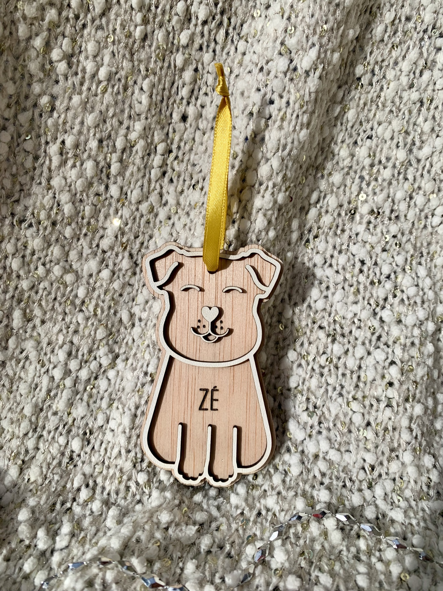 Enfeite de madeira em forma de cão com fita amarela sobre manta gris