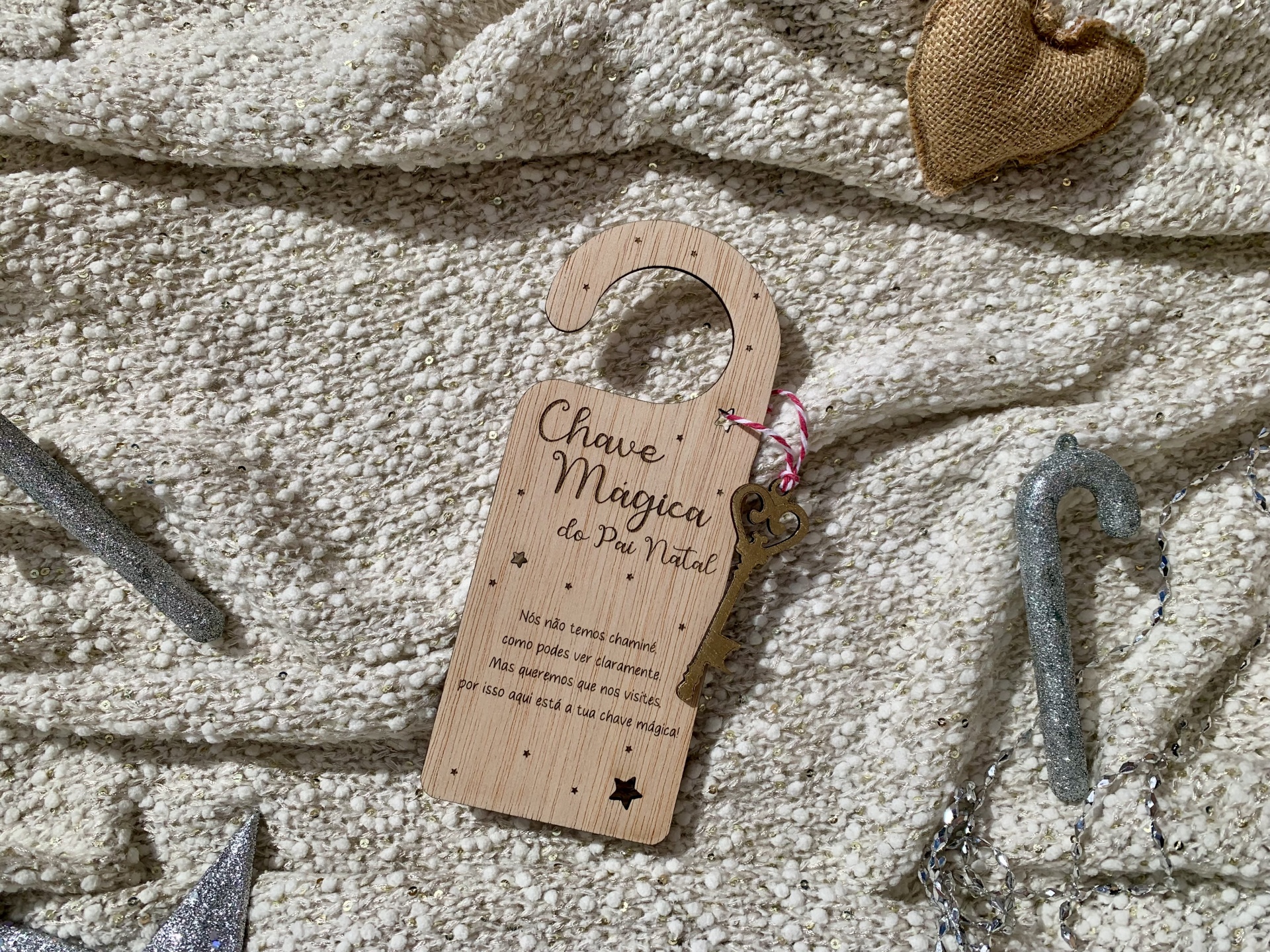 Gancho decorativo de madeira com texto sobre fundo têxtil e enfeites natalícios