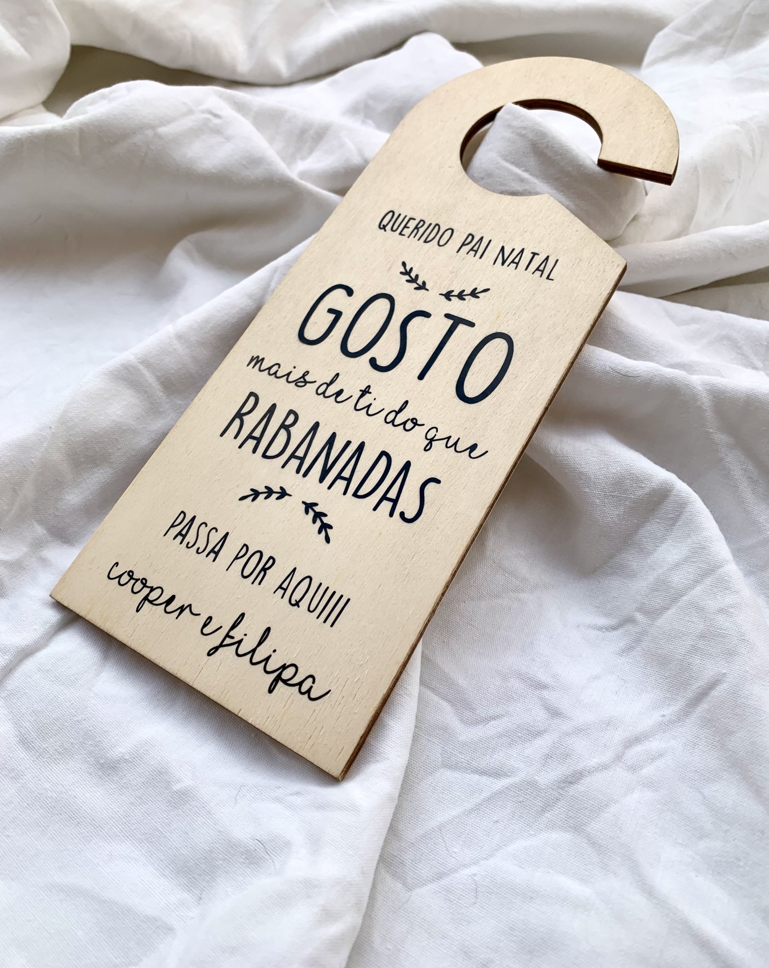 Placa pendente de madeira clara com texto em preto colocada sobre tecido branco