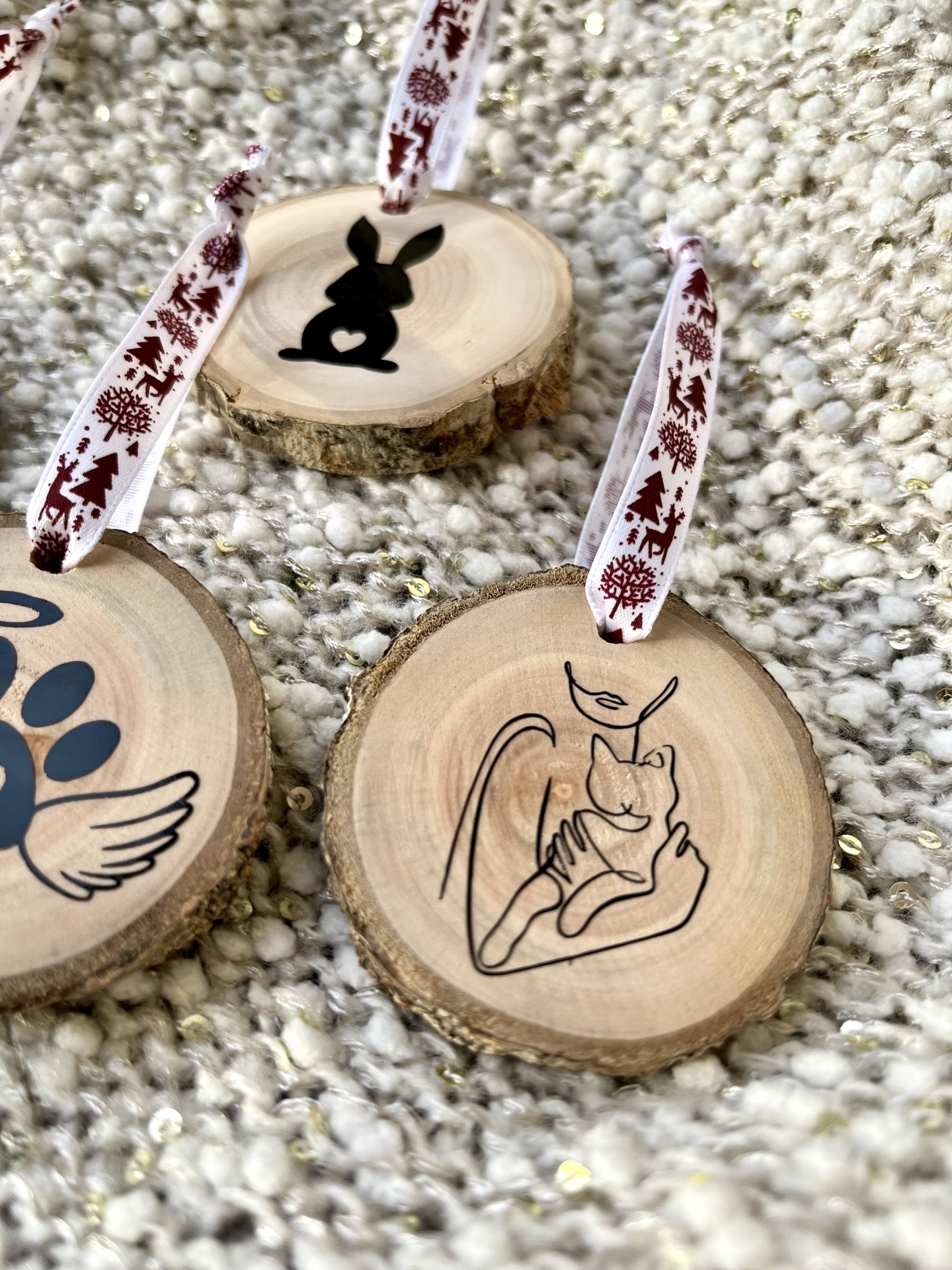 Enfeites redondos de madeira com desenhos a preto e fitas festivas em fundo branco texturado.