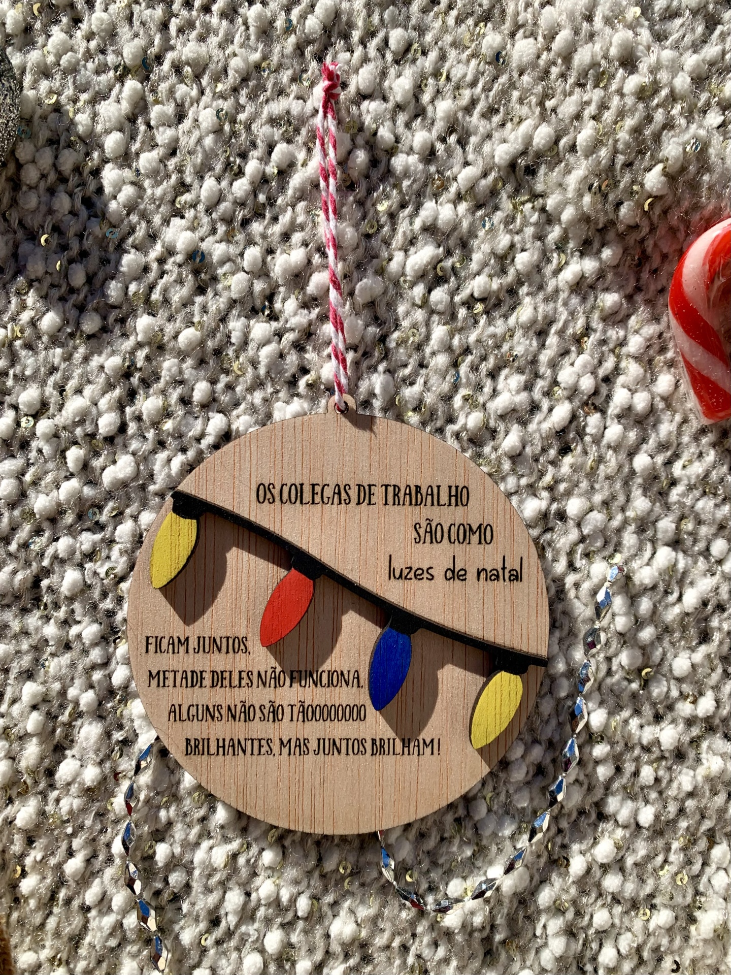 Plaquinha redonda de madeira com mensagem e luzes de Natal coloridas pendurada