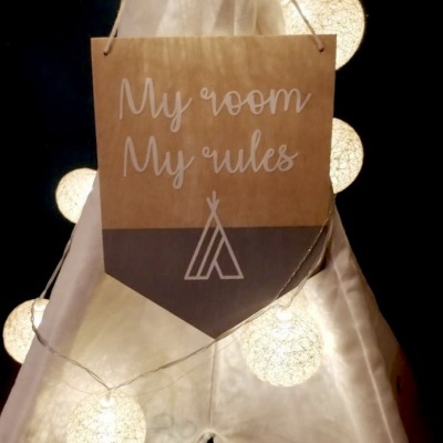 Painel decorativo em papel castanho pendurado num tecido branco semelhante a um tipi, iluminado por luzes brancas redondas.