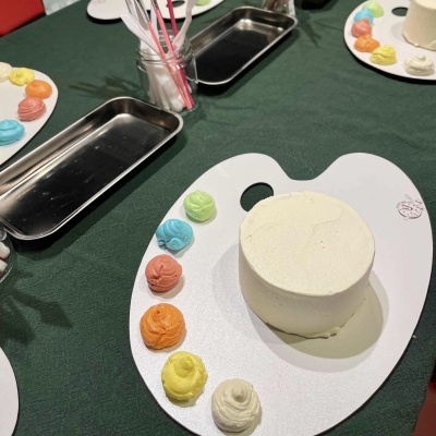 Bolo branco pequeno com várias cores de creme em paleta de pintura sobre mesa