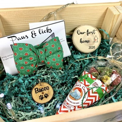 Caixa de presente com gravata borboleta verde com morangos, biscoitos decorativos com texto Our first home 2020 e Bacco, e petiscos para cães.