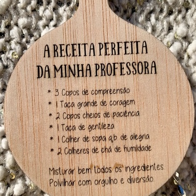 Tábuas de madeira com texto gravado 'A RECEITA PERFEITA DA MINHA PROFESSORA' sobre tecido felpudo