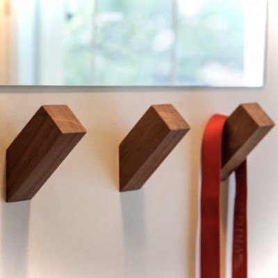 Três ganchos de parede em madeira com um cinto vermelho pendurado.