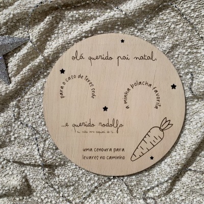 Placa redonda de madeira com texto e desenhos gravados em preto sobre tecido bege com textura e estrela prateada ao lado