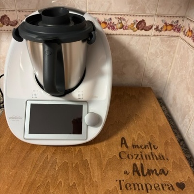 Robot de cozinha branco com jarra metálica e superfície de madeira com texto gravado.