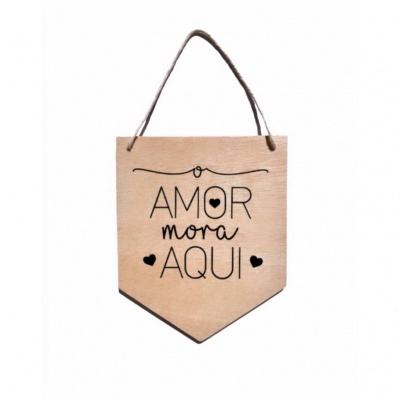 Placa decorativa de madeira clara com texto 'O AMOR mora AQUI' em preto e corda para pendurar