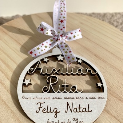 Enfeite de Natal redondo em madeira clara com texto e estrelas recortadas, pendurado em laço decorativo