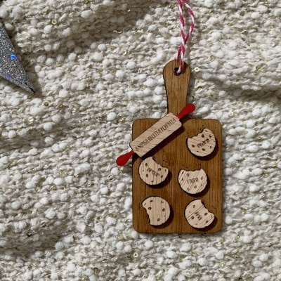 Enfeite decorativo em madeira com cookies e rolo de massa pendurado sobre tapete claro texturizado