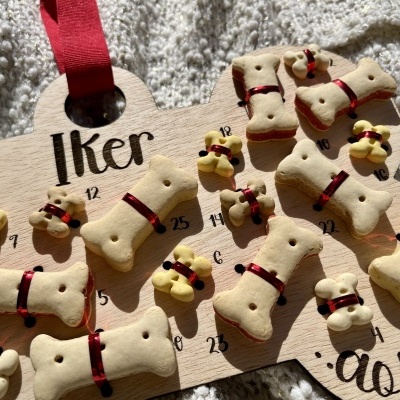 Calendário de advento em madeira com biscoitos de cão em forma de ossos amarrados com fita vermelha e números escritos.