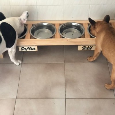 Comedouro duplo para cães de madeira com duas tigelas de metal e etiquetas com nomes Safira e Bált, cão a comer em cada lado