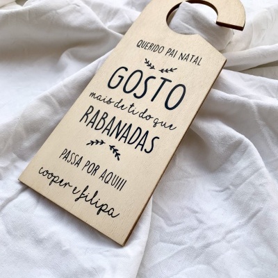 Placa pendente de madeira clara com texto em preto colocada sobre tecido branco