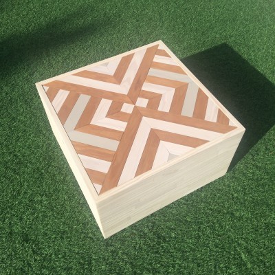 caixa quadrada de madeira com tampa geométrica em cima de relva artificial
