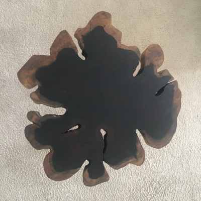 Mesa de centro de madeira maciça escura com formato irregular sobre tapete claro