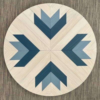 Mesa redonda de madeira clara com padrão geométrico azul sobre tapete castanho