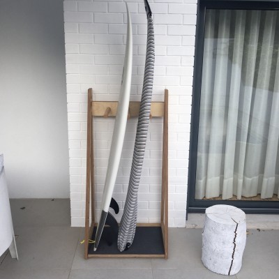 Suporte com duas pranchas de surf junto a parede branca e janela com cortinas brancas