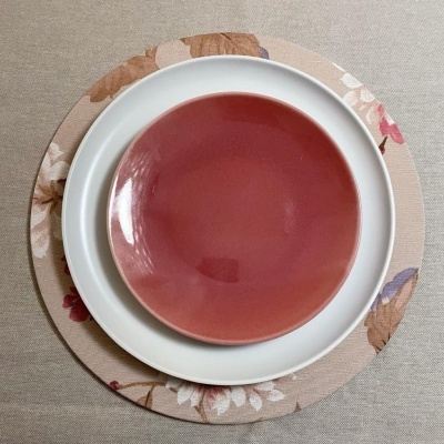 Três pratos cerâmicos empilhados em cima de tecido bege, com o prato maior floral, o médio branco e o pequeno vermelho.