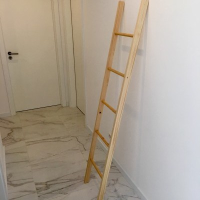 Escada de madeira clara encostada a parede branca num corredor com chão de azulejos brancos