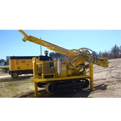 Máquina perfuradora amarela com estrutura metálica e lagartas pretas em terreno aberto