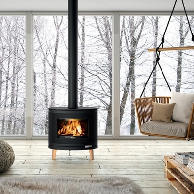 Lareira a lenha preta com pernas de madeira clara junto a janela com vista de árvores e cadeira suspensa