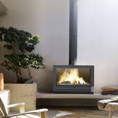 Lareira moderna a lenha com fogo no interior em parede branca com planta e cadeira rústica