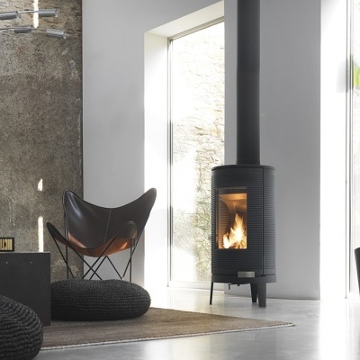 Lareira a lenha preta junto a cadeira em couro e pufes pretos em ambiente com grande janela