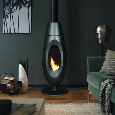 Lareira suspensa oval em metal preto numa sala moderna com sofá verde e parede cinzenta.