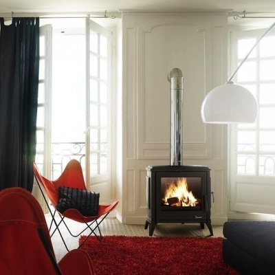 Sala com lareira, cadeiras laranja, tapete vermelho, cortinas pretas e candeeiro branco