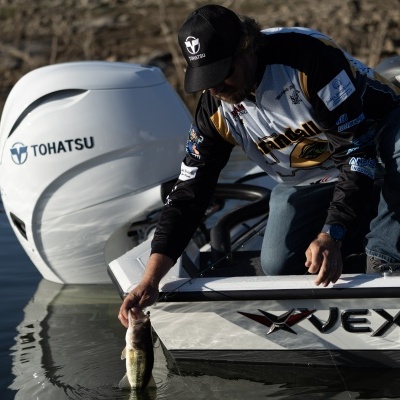 Barco branco Vexus com motor de popa Tohatsu e homem a segurar peixe junto à água