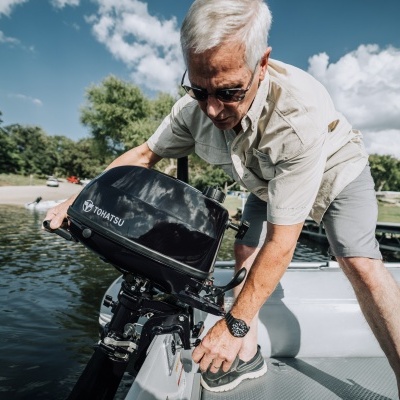 Homem idoso ajustando motor de popa preto TOMCATU numa embarcação inflável