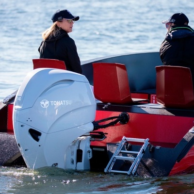 Barco vermelho com motor de popa branco Tohatsu e duas pessoas a bordo.