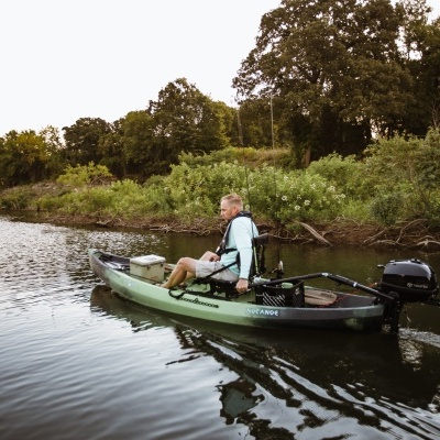Homem a remar caiaque verde com motor elétrico num rio calmo com vegetação