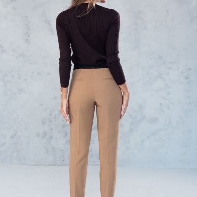 Mulher de costas com camisola preta e calças bege em fundo cinzento claro