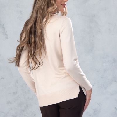 Mulher de costas com camisola bege de manga comprida e calças pretas, fundo cinzento