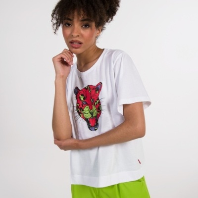 Pessoa a usar t-shirt branca com estampa de cabeça de gato colorida e calças verdes fluorescentes