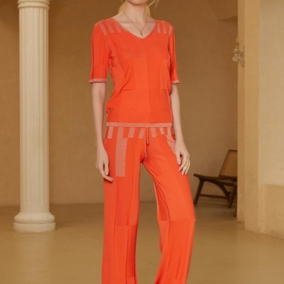 Conjunto de t-shirt e calças largas laranja com detalhes bege, padrão geométrico, tecido suave, usado por modelo em ambiente interior minimalista.