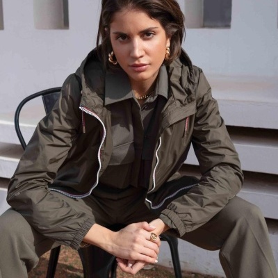 Mulher com casaco e calças verdes sentada numa cadeira preta ao ar livre