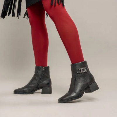 Botins pretos de pele com salto baixo e detalhe metálico em fundo neutro